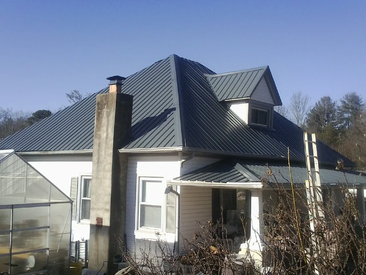 Dark blue standing seam metal roof on a white farmhouse with dormer — Slate & Tile Roof Repair by Roofing Brothers in Freeland