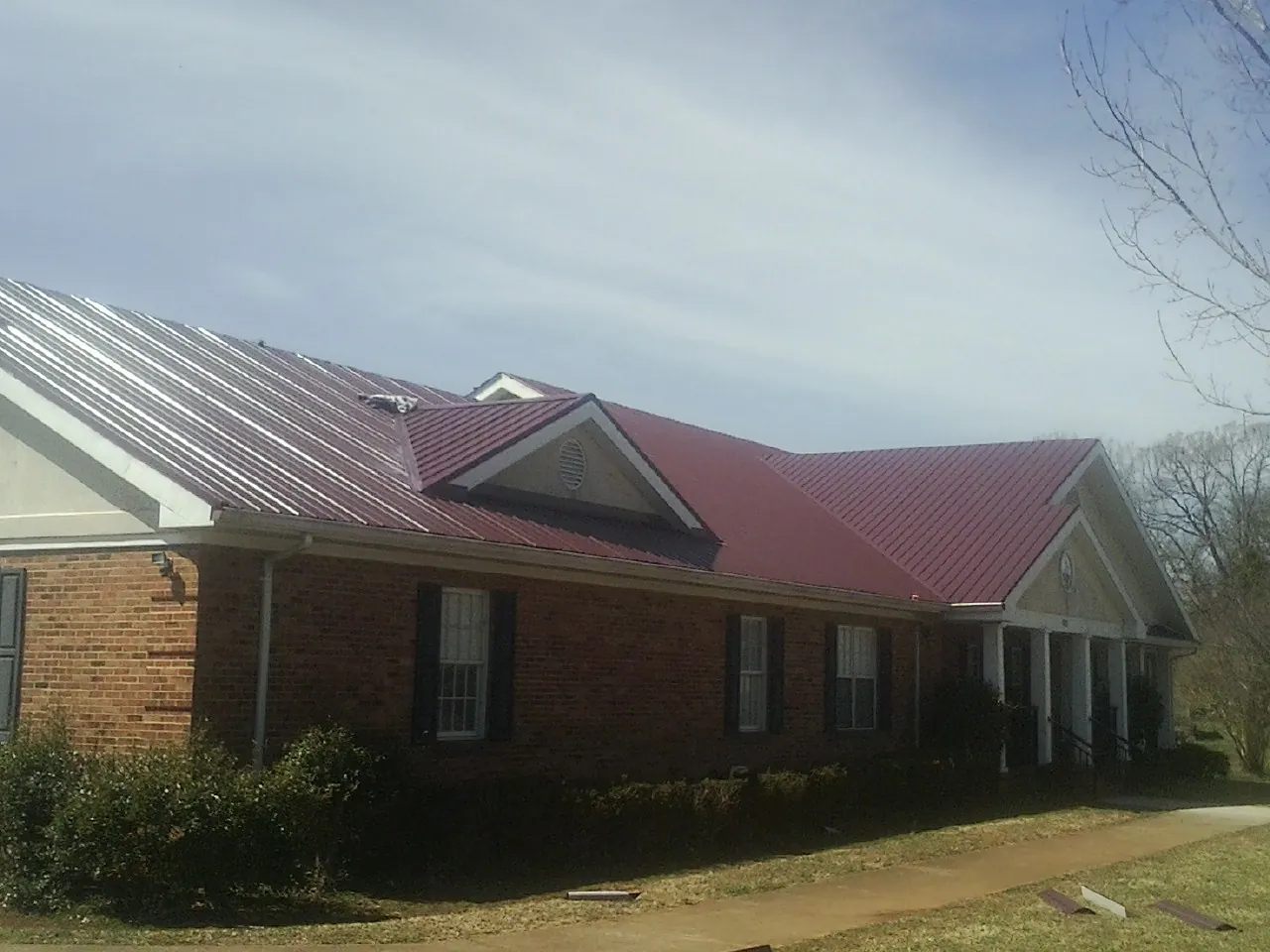 Red metal roof with gabled entries on a long brick building, from a Hail Damage Roof Repair job in Freeland