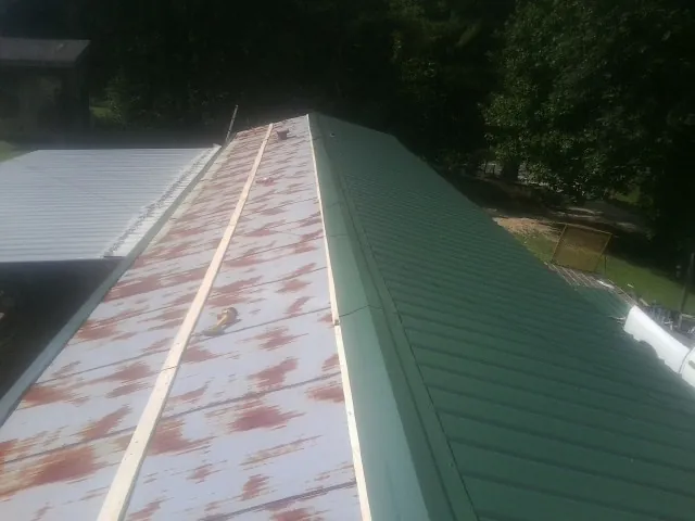 Old rusted panels beside newly installed green metal roofing — Wind Damage Roof Repair by Roofing Brothers in Freeland